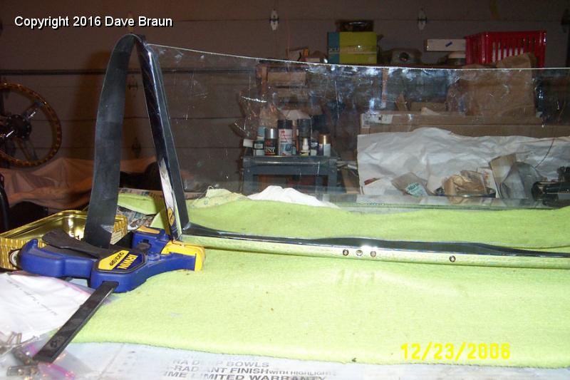 glass slipping into place.jpg - windscreen glass going in. A good view of the padded clamp attached to the hood post. The clamp provided a perfect support, one on each side, to allow testing fit of all the hardware and muscling in the windscreen glass.